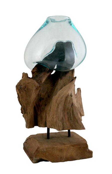 This 12” tall handblown glass and teak wood sculpture has been handcrafted by skilled artisans who have a love for the art of glass blowing. Recycled glass is blown onto the shape of the teak wood root and begins to flow and cradling the form of the wood to create a bowl that is a unique, one of a kind, piece that can be used as a vase, terrarium or fishbowl.
