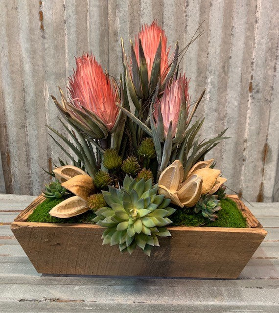 Our Botanical and Succulent Barnwood Bowl Floral Arrangement is a custom made to order arrangement featuring red botanical flowers mixed with pods and succulents and planted in a large recycled and reclaimed barnwood bowl. It is a magnificent arrangement and certainly will make a statement.   The dimensions are approximately 18" L x 20"H x 7"D, based on the barnwood and floral materials.
