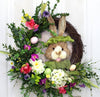 Our Bowtie Bunny Spring Front Door is 23” in diameter and features an array of colorful spring silk flowers as well as a festive bunny rabbit all dressed up with green brim hat and matching bowtie on an exposed grapevine base.