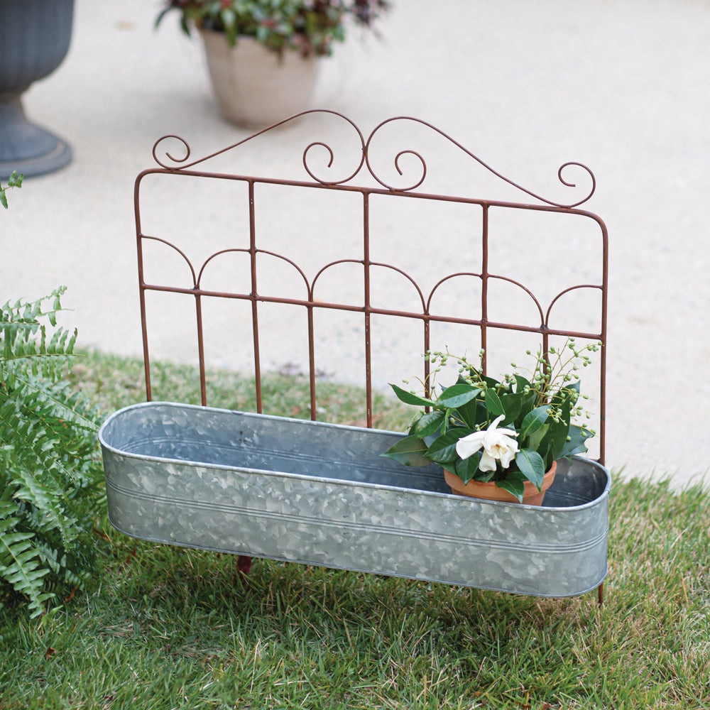 Our Metal Garden Fence Planter is made of wrought iron with an inground stake and resembles a garden fence. The planter bucket is made of galvanized steel and the contrasting color of the rust and silver is so pretty. This versatile planter can be used inground or hung on a wall or fence for a whole new look. Picture shows the planter staked in the ground.