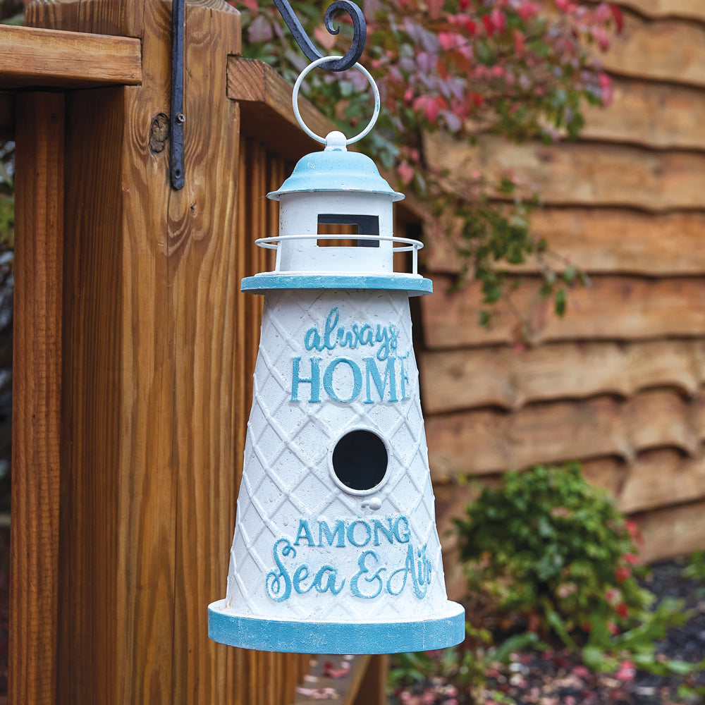 Invite birds into their new nesting home with our Nautical Lighthouse Always Home Birdhouse. It has the verbiage Always Home, Among Sea and Air and has been uniquely crafted of metal, painted in nautical soft blue and white tones, and ready for hanging by the O-ring at the top of the bird house. Size is 8'' dia. x 16'' tall.