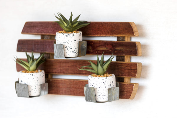Our Reclaimed Wine Barrel Staves Slatted Wall Garden Planter is a unique creation for growing plants indoors and outdoors. Made in the USA by skilled artisans who have disassembled a wine barrel and using the staves, they have made them into a slotted wall décor piece and then added the original metal wine barrel rings to create plant holders.