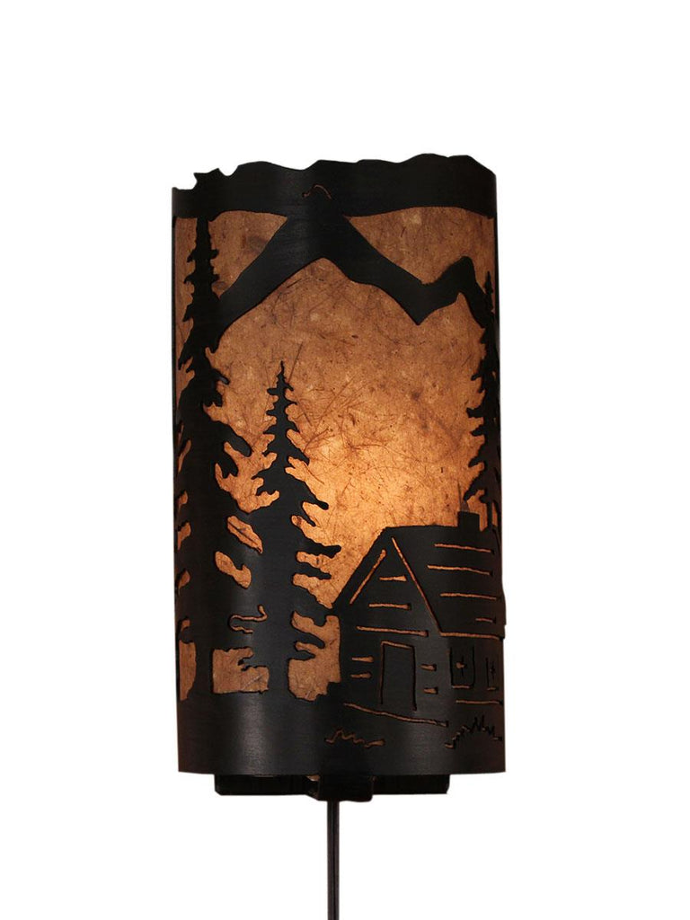 Our Rustic Cabin Panel Wall Sconce captures the forested beauty with cutouts of a metal cabin and trees in front of the amber parchment paper shade