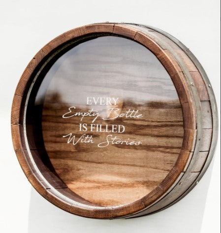 Shown in our walnut stain, this wall mountable Wine Barrel Head Cork Holder has been etched with Every Empty Bottle Is Filled With Stories. It is 21” in diameter x 7” deep and handcrafted, here in the USA, from the use of reclaimed and repurposed wine barrels, wine staves, barrel bands, and clear Plexiglas front, enabling you to view your collection of corks.  You can personalize the front of the Plexiglas with this memorable quote or a memorable quote of your choice.